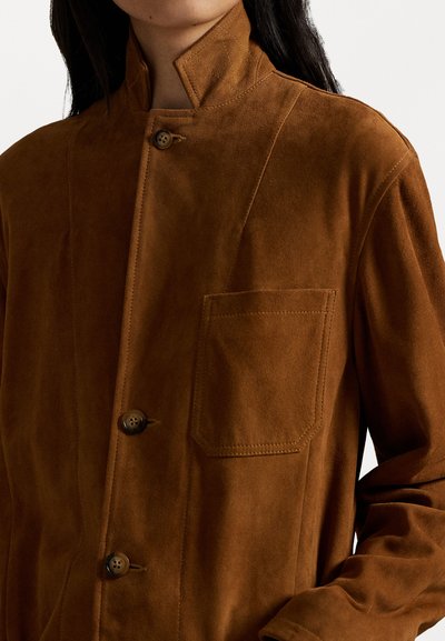 Giacca in suede marrone con colletto alto, dotata di chiusura a bottoni e tasca sul petto. Tessuto liscio e linee pulite.