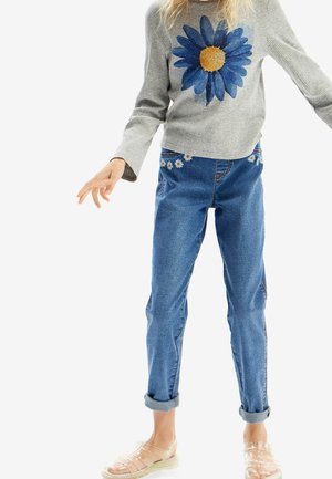 Gray ribbed sweater with blue daisy design, paired with rolled-cuff blue jeans featuring embroidered daisies along the waistband. Clear sandals.