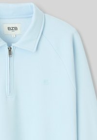 Pull léger bleu clair à manches longues avec un col, demi-zip à l'avant et petit logo embossé sur la poitrine, taille large, marque BZB.
