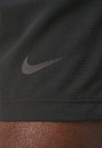 Logo Nike imprimé sur un tissu noir texturé d'une manche au-dessus d'un poignet à peau foncée.