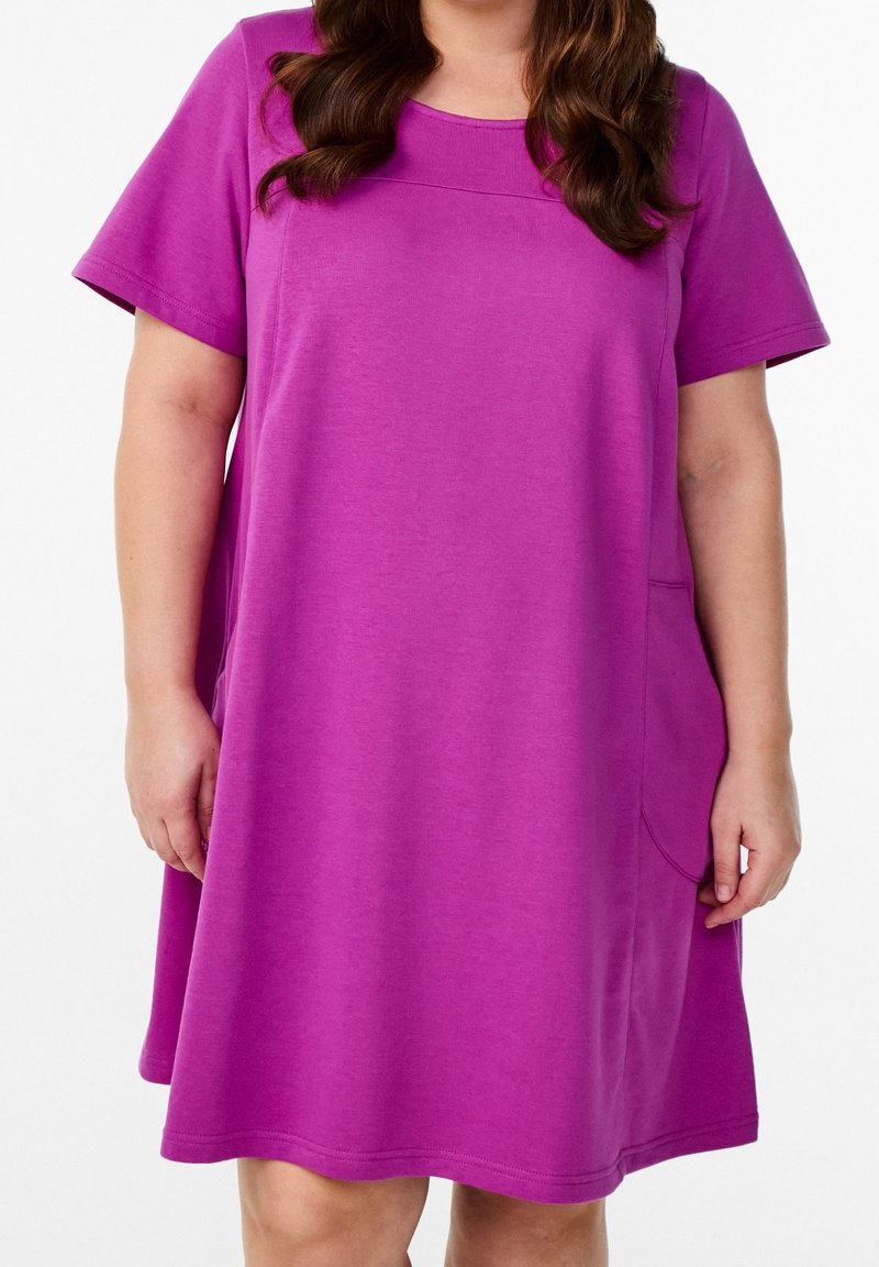 Femme portant une robe magenta ample à manches courtes avec un col rond et une poche sur le côté droit.
