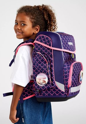 Purple backpack with pink scalloped pattern, reflective accents, and circular badges. Features padded straps and multiple compartments for storage.