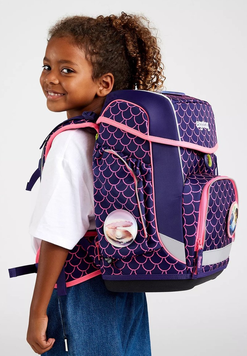 Purple backpack with pink scalloped pattern, reflective accents, and circular badges. Features padded straps and multiple compartments for storage.