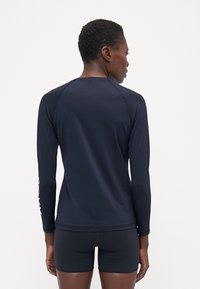 Juodas ilgomis rankovėmis rash guard'as su plokščiais siūlės, sukurtas pritaikyti patogumui ir pritaikymui. Medžiaga atrodo lygi ir elastinga, tinkama vandens veikloms.