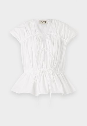 Hvid bomuldsbluse med korte puffærmer, rynket detaljer og sløjfefront. Peplum-forneden tilføjer en svajet silhuet. Mærkets label er synlig.