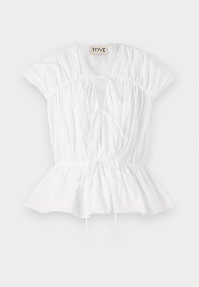 White cotton blouse with short puff sleeves, gathered detailing, and a tie front. Peplum hem adds a flared silhouette. Brand label visible.