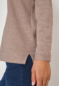 Maglietta a maniche lunghe in morbido tessuto a coste beige con spacchi laterali e scollatura rotonda, abbinata a jeans blu scuro.