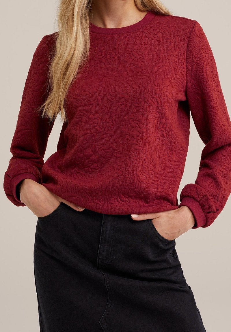 Bordeaux Sweatshirt mit strukturiertem Blumenmuster, Rundhalsausschnitt und gerippten Bündchen, kombiniert mit einem schwarzen Jeansrock. Weicher, warmer Stoff.
