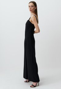 Zwarte jumpsuit met dunne bandjes, aansluitende pasvorm en wijde pijpen. Soepele textuur en minimalistisch ontwerp. Zwarte hoge hakken maken de look compleet.