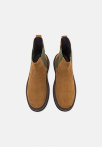 Bottines en daim marron avec accents en textile vert, design sans lacets, bout arrondi et semelle en caoutchouc noire. Équipées d'une languette à tirer pour un enfilage facile.