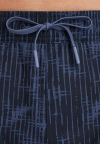 Shorts de bain marine avec un motif texturé de lignes verticales et horizontales. Dotés d'une taille élastique avec un cordon de serrage pour un ajustement réglable.