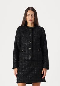 Mustat tweed-takit, jossa on tekstuuri, pyöreä kaula-aukko ja seitsemän metallipainiketta. Sisältää kaksi etutaskua. Mukautettu istuvuus.