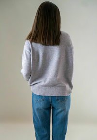 Grijze gebreide trui met ribbelzoom, gecombineerd met lichtblauwe denim jeans. Het zicht toont de achterkant van de outfit en benadrukt de eenvoud ervan.