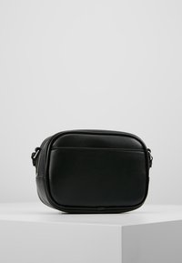 Czarna torba na ramię wykonana z gładkiego materiału syntetycznego. Kwadratowy kształt z zamkiem błyskawicznym i prostym, minimalistycznym wyglądem. Regulowany pasek.