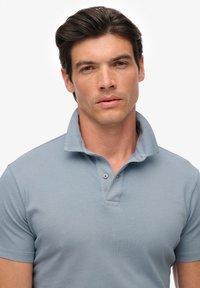 Jasnoniebieska koszulka polo wykonana z bawełny, z klasycznym kołnierzykiem, dwu guzikowym zapięciem i krótkimi rękawami. Gładka tekstura z minimalnymi akcentami.
