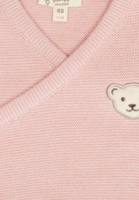 Světle růžový pletený svetr s výstřihem do V, se malou vyšitou tváří medvídka na přední straně. Vyrobeno z organického materiálu.