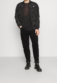 Czarna kurtka puchowa z prążkowanymi mankietami, połączona z czarnym t-shirtem i czarnymi spodniami sztruksowymi. Czarne botki o gładkiej fakturze.