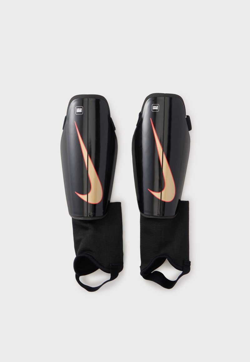 Ζευγάρι μαύρα προστατευτικά κνήμης Nike με μπεζ και κόκκινο λογότυπο Swoosh, διαθέτουν συνδεδεμένα μαύρα μανίκια αστραγάλου με ιμάντες.