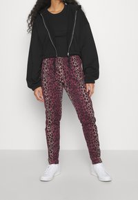 Černá krátká mikina na zip vpředu, ve spojení s růžovými kalhotami s leopardím potiskem. Bílé tenisky doplňují outfit a zdůrazňují živé vzory.