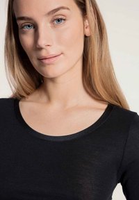 Black long-sleeve top with a round neckline, featuring a smooth texture and a subtle sheen at the collar. Close-up of fabric and design details.