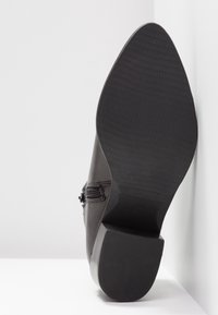 Botín negro de cuero hasta el tobillo con suela texturizada, forma cónica y detalle de cremallera lateral. El tacón plano ofrece estabilidad y comodidad.