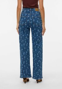 Szerokie dżinsy z niebieskiego denimu w kwiatowy wzór, z wysokim stanem, ozdobione brązową skórzaną metką z tyłu oraz dwoma tylnymi kieszeniami.