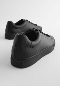 Svarta lädersneakers med en slät yta, rund tå, platta snören och lågprofill gummisula med ett mönstrat grepp.