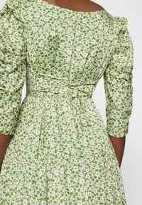 Green floral dress with a fitted bodice, puffed sleeves, and a tie waist. The design features white flowers on a green background.