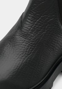 Černá kotníková bota z kůže s texturovaným povrchem, pružnými bočními panely a nízkým podpatkem. Viditelný je zaoblený špička a hladký obrys podrážky.