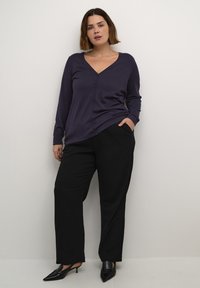 Cardigan lung cu mânecă lungă de culoare violet închis, cu decolteu în V, închidere cu nasturi și o croială relaxată, asociat cu pantaloni negri cu picioare largi și tocuri negre ascuțite.