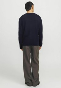 Suéter de punto azul marino con mangas largas y escote redondeado, combinado con pantalones grises de corte holgado y botas negras. Se muestra vista posterior.
