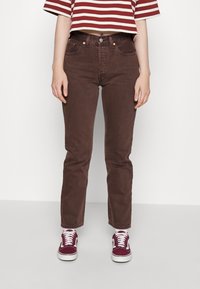 Bruna denimjeans med rak passform, fem fickor och synliga sömmar. Matchas med en röd- och vitrandig kort topp och burgunderfärgade sneakers.