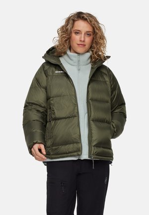 Groene pufferjack met een capuchon, met een doorgestikte ontwerp, zijzakken en een ritsluiting. Draagt over een lichtgrijze fleecetop.