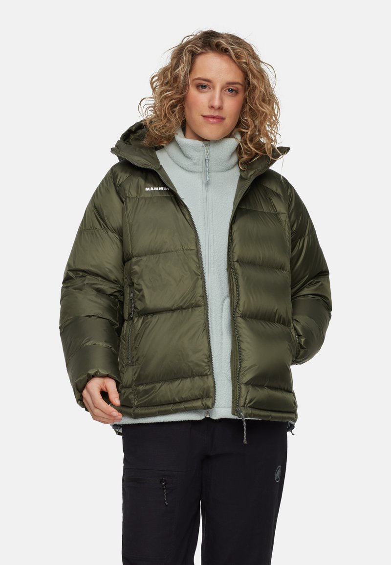 Groene pufferjack met een capuchon, met een doorgestikte ontwerp, zijzakken en een ritsluiting. Draagt over een lichtgrijze fleecetop.