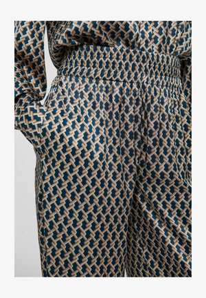 Pantalon à motifs en tissu lisse présentant un design géométrique en bleu marine, crème et marron clair, avec une taille élastique.