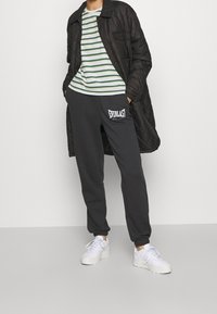 Černá prošívaná bunda, bílé a zelené pruhované tričko, tmavě šedé tepláky s logem "Everlast" a bílé tenisky. Neformální outfit.