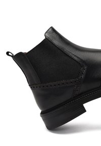 Botín negro de cuero con un acabado suave, un diseño con costuras y detalles perforados, y suela de goma con borde estriado.