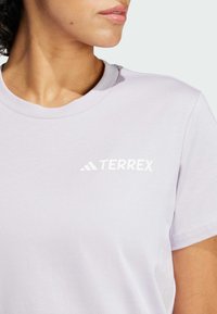Světle levandulové tričko vyrobené z bavlny s kulatým výstřihem. Na levé části hrudi se nachází bílé logo "TERREX". Hladká textura.