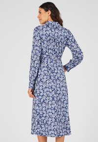 Abito a maniche lunghe in blu navy con motivo floreale bianco. Presenta un colletto e una vita aderente, che si sviluppa in una gonna di lunghezza al ginocchio.