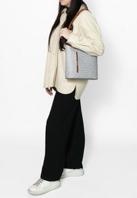 Sac fourre-tout gris avec une surface texturée, des accents marron et une fermeture éclair sur le côté. Associé à une chemise oversized crème et un pantalon large noir.