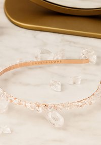 Serre-tête en or rose avec des accents de cristal clair le long du bord avant. Bande texturée avec "CRYSTALLOVE" gravé sur le côté intérieur.