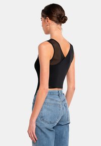 Svart ärmlös topp med meshrygg, tight passform och korsettsnittsdesign. Kombinerad med högmidjade denimjeans med ljus tvätt.