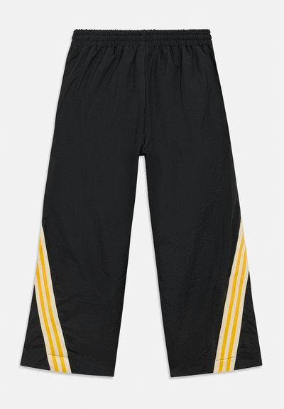 Svarte joggebukser med elastisk midjebånd og to gule striper på siden. Laget av et lett, glatt stoff.