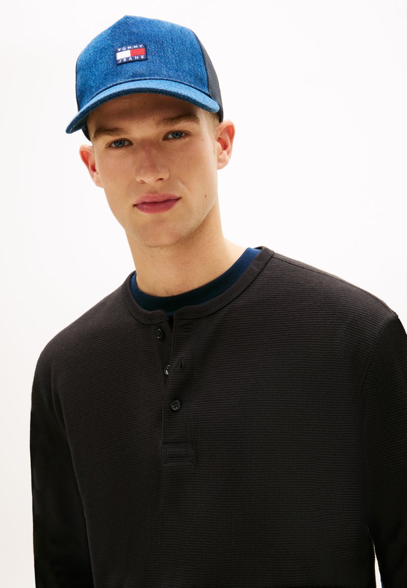 Μαύρο μακρυμάνικο πουκάμισο henley με υφή ύφασμα και τρία κουμπιά, σε συνδυασμό με μπλε τζιν καπέλο που διαθέτει λογότυπο.