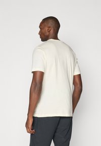 Short-sleeve light beige t-shirt made of cotton, featuring a crew neck and relaxed fit, shown from the back against a neutral background.