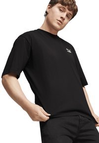 Maglietta nera a maniche corte in cotone, con un logo bianco discreto sul petto. Il tessuto appare liscio e ha una vestibilità comoda.