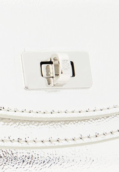 Ασημένιο μεταλλικό κούμπωμα με περιστροφικό κλείδωμα σε υφή λευκού δέρματος με λεπτομερείς ραφές.