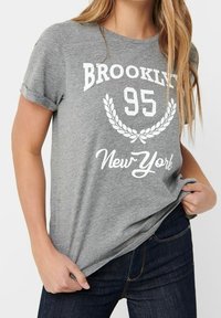 T-shirt grigio in cotone con maniche arrotolate, con la scritta bianca "Brooklyn 95" e una grafica di alloro, completata dalla scritta "New York" in corsivo.