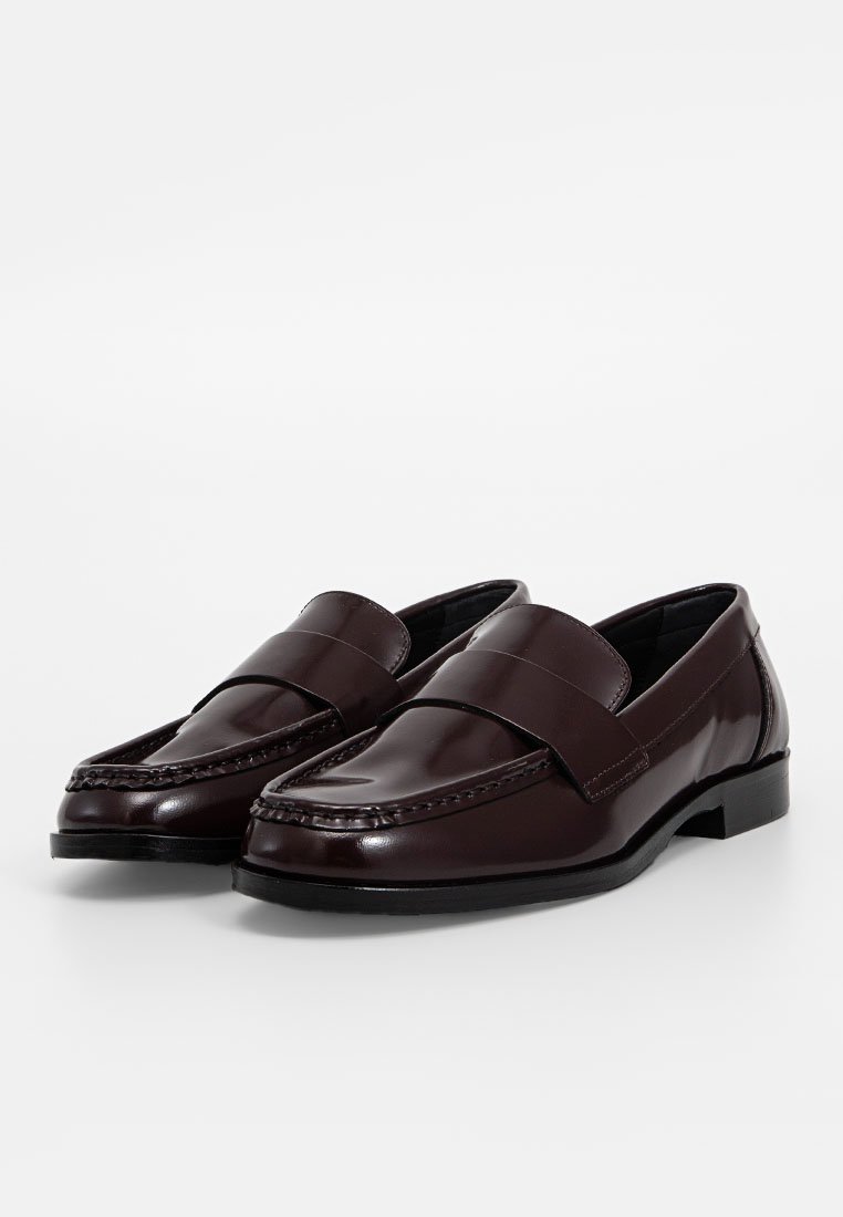 Ciemnobrązowe skórzane loafersy o gładkim wykończeniu, z przeszyciem i płaskim obcasem. Projekt zawiera szeroki pasek z przodu.