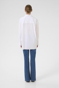 White long-sleeve shirt with a button-up collar, featuring a single back yoke and a relaxed fit. Paired with blue flared jeans.